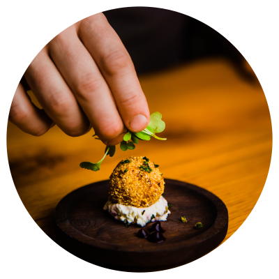 An arancini being topped with microgreens by the chef