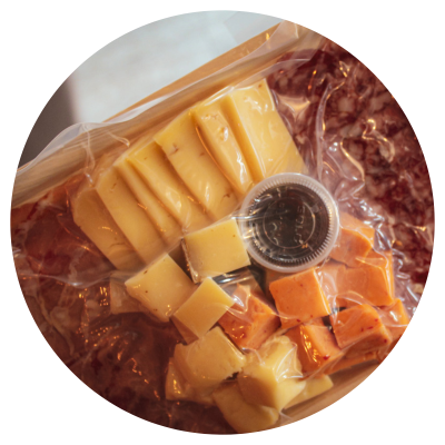 Vacuum sealed charcuterie plate with a selection of cheeses, meats, and jelly.