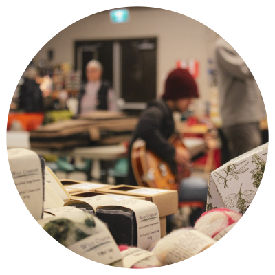 Natural body care item booth in foreground with local musicians playing at the farmers market in background