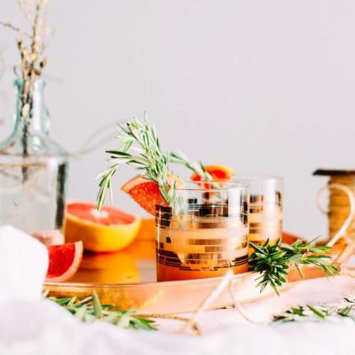Drinks a copper tray on a table with fruit and rosemarry as garnish