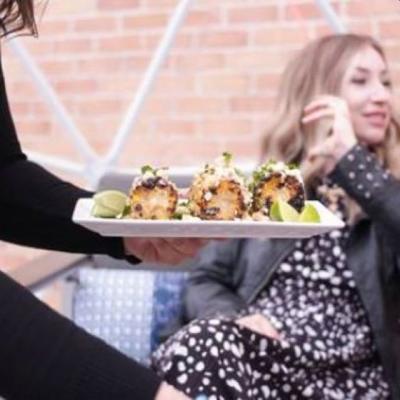 A photo of grilled corn on the cob being served to a table of people