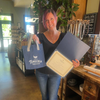 Sara Cox posing with a Temecula tote bag and a certificate.
