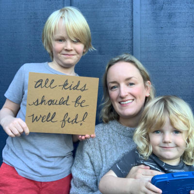 Fanny Adams of Trout Lily Ranch and children hold sign saying "all kids should be well fed"