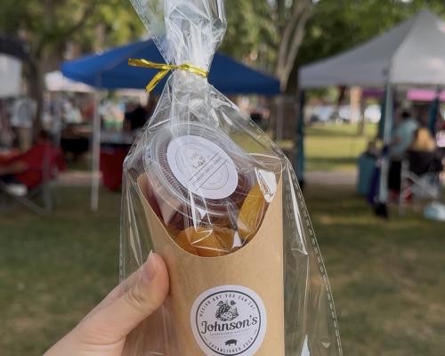 A hand holding a box of goodies in front of the Historic New Castle Farmers Market.