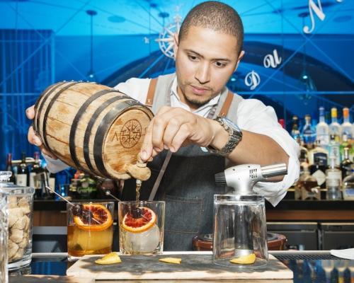 Bartender pouring liquor from the spout of a barrel into a craft cocktail glass