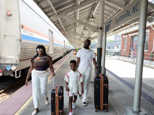 A family walks along the Fayetteville, NC Amtrak platform with luggage, arriving for their trip.