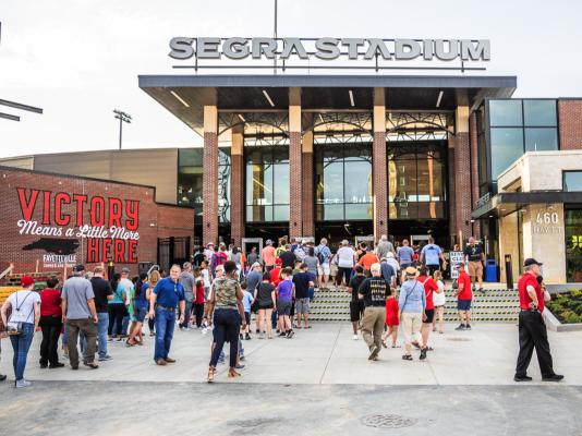 Image of a crowd milling around Segra Stadium courtyard/entrance with mural "Victory Means a Little More Here"