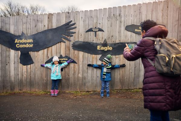 Two children and a mom at the Zoo taking a photo with the bird wingspans