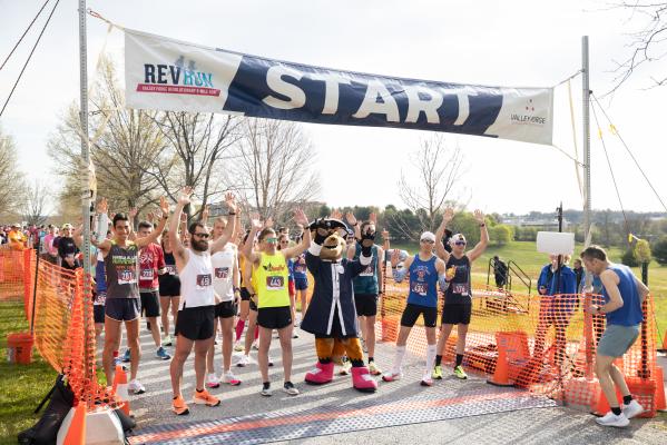Runners raise their arms with the VFTCB mascot, Monty at the starting line for the 2022 Rev Run