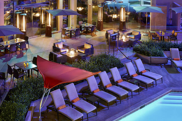 Image of the pool area at the Anaheim Marriott. Image is of a portion of the pool surrounded by eight pool lounge chairs, with restaurant tables in the background.