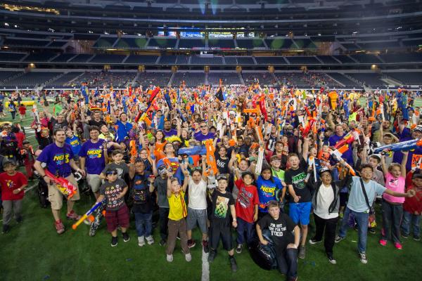 Kids and adults on a field inside a stadium holding nerf guns 