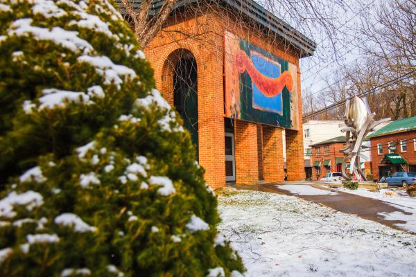 A snowy tree can be seen in front of a building with a large piece of art on the front.