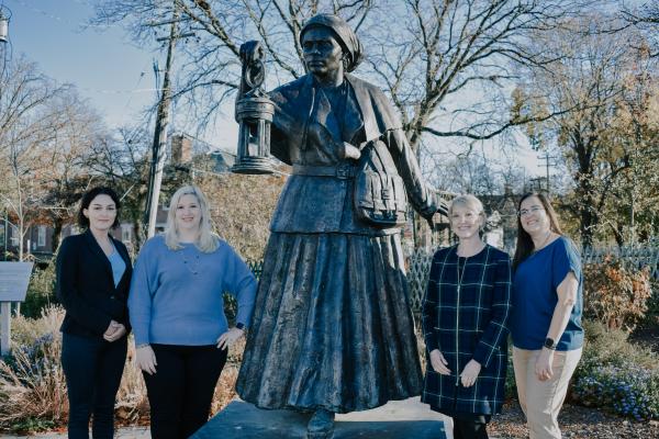 4 women standing outside in front of a bronze statue of Harriet Tubma
