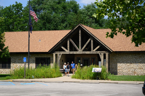 Family walking out of the rustic stone visitor center at Charlestown State Park on a sunny summer day, with American and Indiana flags flying outside.