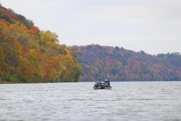Two people boating on the Ohio River near Charlestown State Park in Southern Indiana, surrounded by forested hills filled with colorful fall foliage.