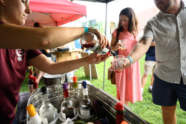Alt text: A vendor pours a wine sample into an attendee’s cup at Distillery 64’s Liquid Legends Fest in Southern Indiana, with bottles of wine displayed at an outdoor tasting booth.