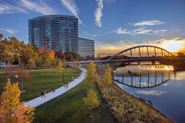 Orange and yellow trees surround the Scioto Mile and a sun sets in the background