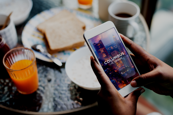 The Columbus Experience App shows on a mobile phone at the breakfast table