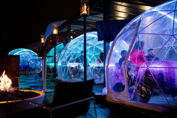 Colorful outdoor igloos lit up with on VASO's rooftop patio with people dining inside