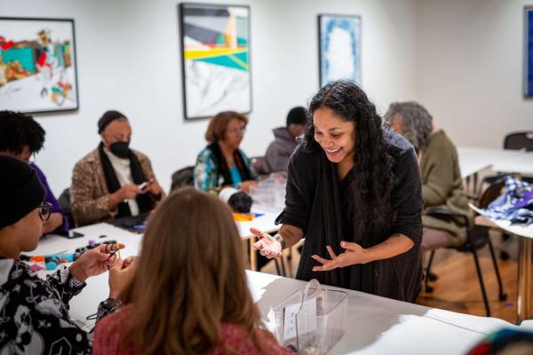 An engaging workshop at the Columbus Museum of Art, where participants of all ages are enjoying hands-on art activities. A smiling instructor interacts with attendees, creating a lively and creative atmosphere. Artwork adorns the walls in the background, adding to the inspiring environment.