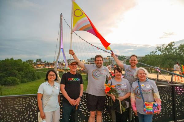 Rainbow Dublin Pride Celebration - A group of individuals holding an LGBTQIA+ flag in front of the Dublin Link Pedestrian Bridge 