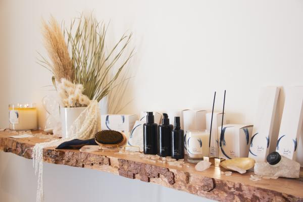 Natural beauty products and candles lined up on natural wood shelf.