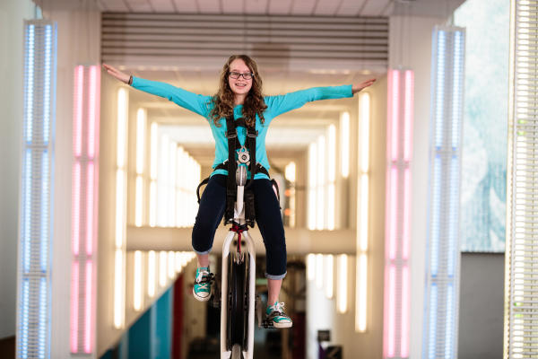 Young girl riding a high wire unicycle inside COSI