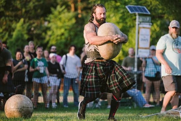 A man in a kilt carrying a large stone in the Stones of Strength competition at the Dublin Irish Festival