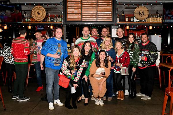 Group of people in festive ugly sweaters posing together at a lively bar during the Ugly Sweater Crawl in downtown Dublin