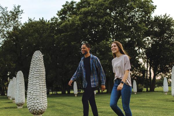 A couple smiling while walking through a field of concrete corn statues.