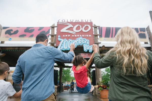A mom and dad swinging their daughter between them at the entrance of the Columbus Zoo