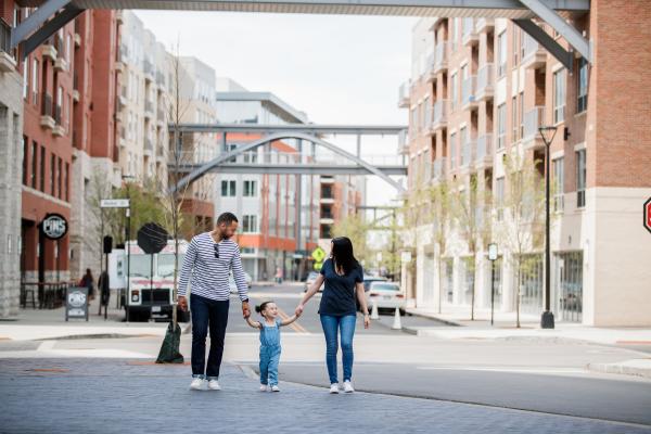 A mom and dad holding handing with their daughter between them in the streets of Bridge Park