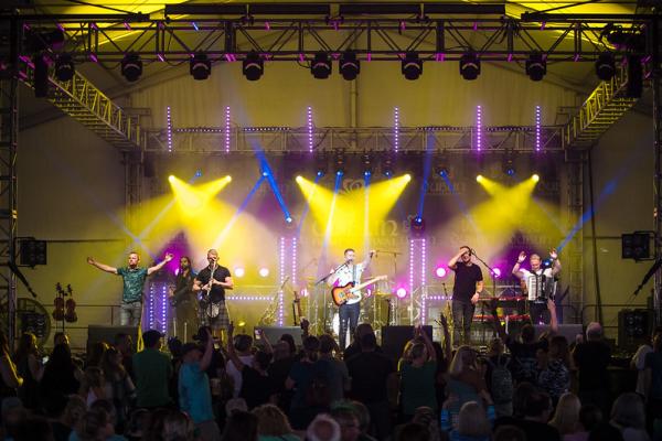 Band performing to a crowd on stage under bright yellow lights on the Celtic Rock Stage at the Dublin Irish Festival