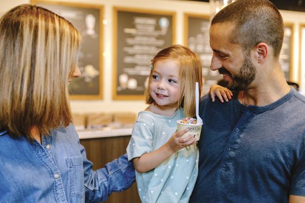 A mom and dad looking at their little girl holding a cup of ice cream at Johnson's Ice Cream