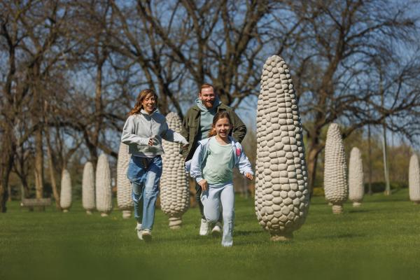 A family runs and laughs together through rows of tall concrete corn sculptures at the Field of Corn in Dublin, Ohio.