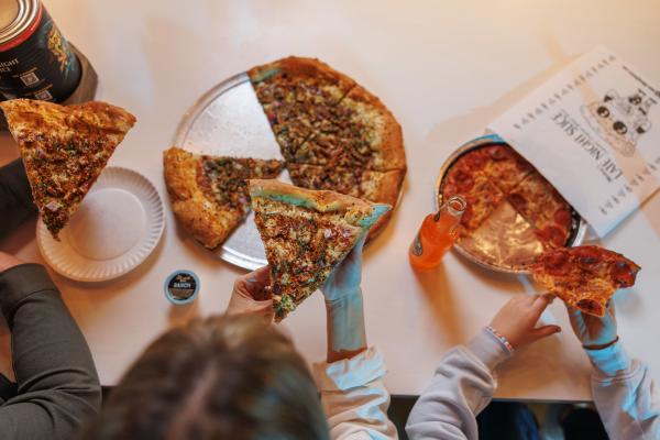 Overhead view of three people enjoying large pizza slices, soda, and ranch dipping sauce at a table with Late Night Slice branding.
