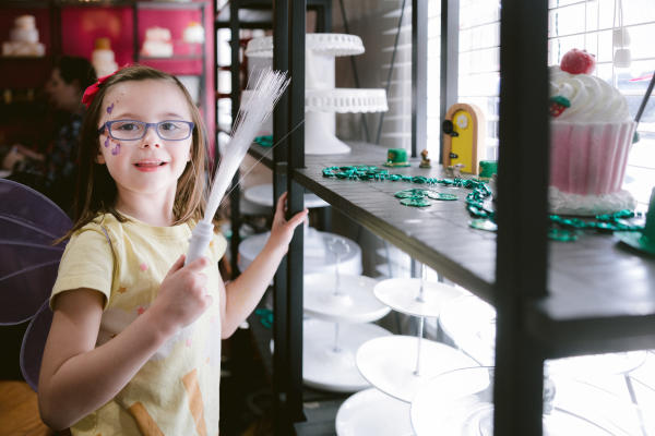 A young girl smiling with a wand and fairy wings looking for the door on the Irish Fairy Door Trail