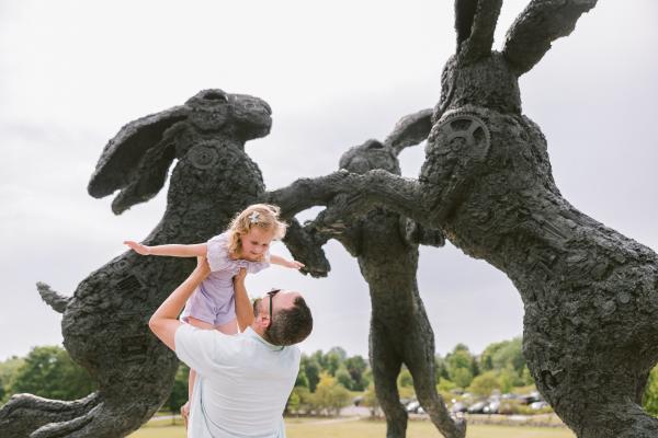 Father lifts smiling daughter near playful bronze rabbit statues at Ballantrae Community Park in Dublin, Ohio.