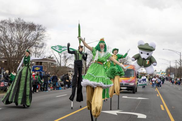 A group of stilt walkers dressed in green performing down the street in the St. Patrick's Day Parade.