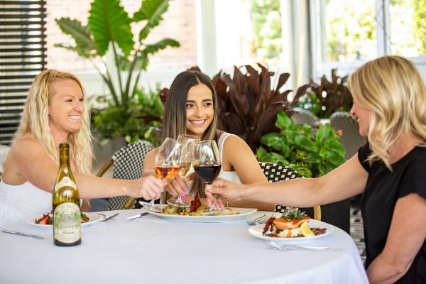 Three women cheersing wine glasses on Tucci's covered outdoor patio