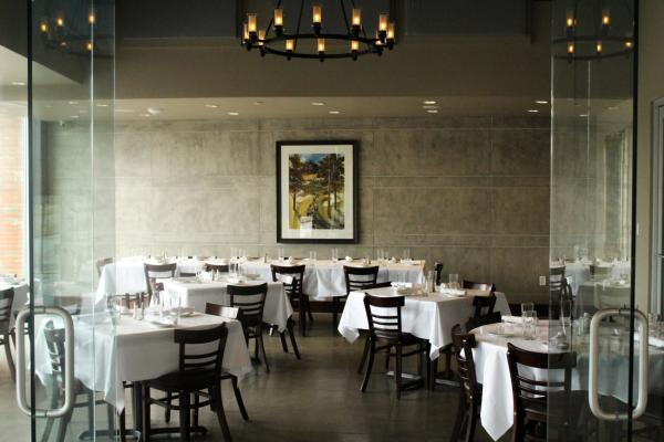 Z Cucina Bridge Park's private dining room with glass walls, a chandelier, and round tables covered in white linens.