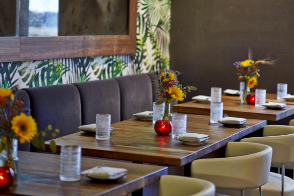 VASO's private dining room featuring wooden tables, fresh flower vases, red candle holders, and cream chairs against tropical leaf-patterned wallpaper.