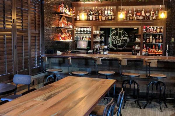 Beer Barrel's private dining room with a full bar with a wooden bar counter, shelves of bourbon bottles, and rustic wooden tables and chairs.