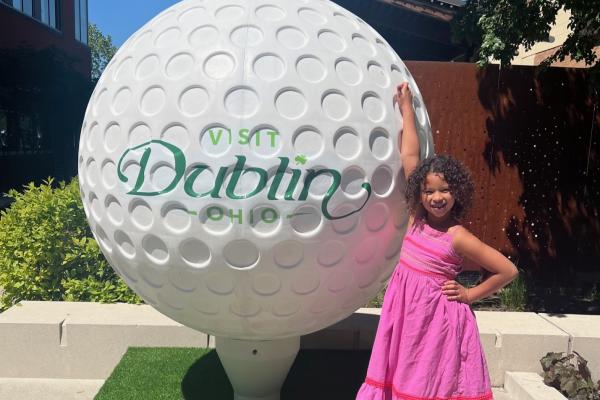 Giant Visit Dublin branded golf ball with young girl posing next to it.