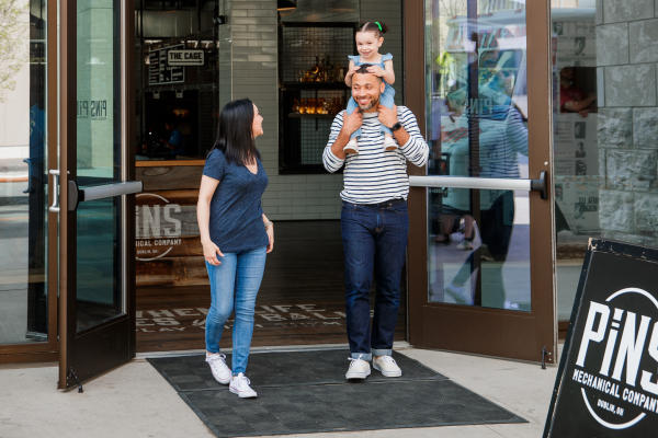 A mother, father and daughter walking out the front of PINS Mechanical with the daughter on the shoulders of the father.