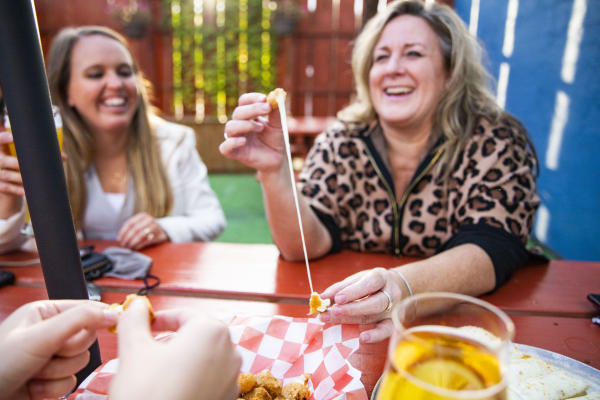 A group of women eating cheese curds and laughing on the outdoor patio at Growler Guys