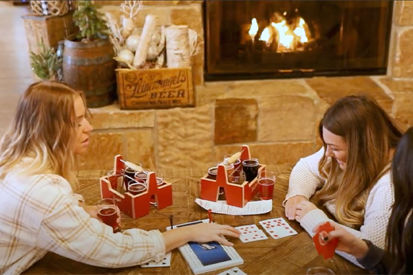 A group of women playing cribbage and drinking flights of beer near the fireplace at Leinie Lodge
