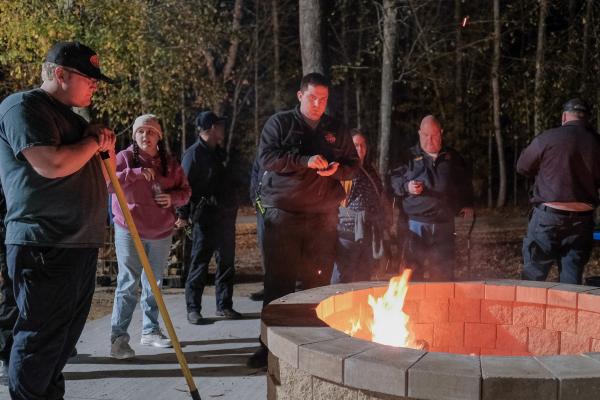 group of men and women hanging out around a firepit watching the fire