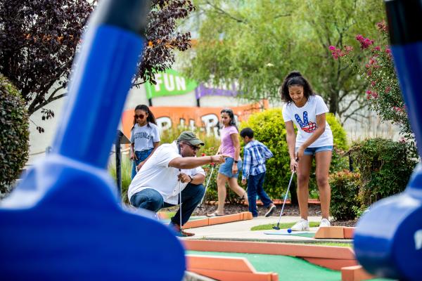 Children and an adult playing mini golf together outdoors during a family-friendly activity