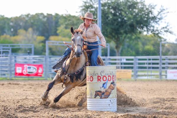 A cowgirl rides a horse around a barrel.